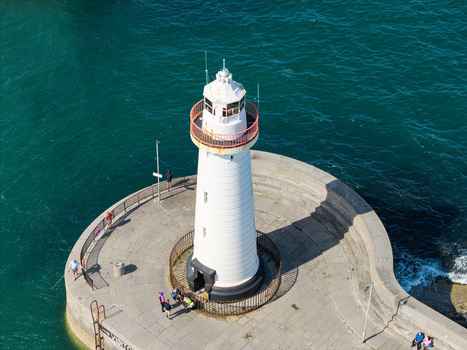 Aerial view of Donaghadee Harbour lighthouse with people walking on the stone pier surrounded by deep blue sea in Donaghadee Northern Ireland United Kingdom. Aerial view of Donaghadee Harbour lighthouse with people walking on the stone pier surrounded by deep blue sea in Donaghadee Northern Ireland United Kingdom.