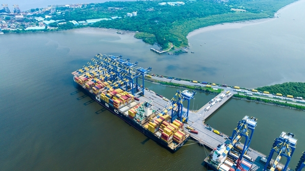 Aerial view of the Jawaharlal Nehru Port Authority container terminal with a large cargo ship gantry cranes and trucks on the access road in Juna Sheva Maharashtra India. Aerial view of the Jawaharlal Nehru Port Authority container terminal with a large cargo ship gantry cranes and trucks on the access road in Juna Sheva Maharashtra India.