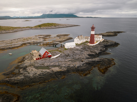 Aerial view of Tranoy Lighthouse situated on a rocky island with red and white buildings a bridge and clear coastal waters in Tranoy Nordland Norway.