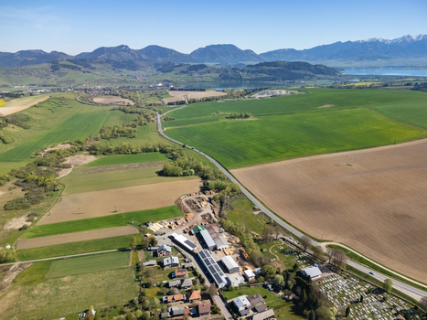 Aerial view of Partizanska Lupca with green fields winding roads and the Tatra mountains under a clear blue sky Partizanska Lupca Zilina Region Slovakia.