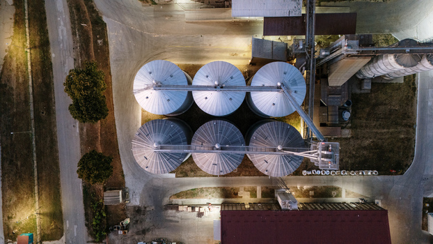 Aerial view of industrial grain silos illuminated at night featuring metallic storage tanks and surrounding facility infrastructure in Sremska Mitrovica Vojvodina Serbia. Aerial view of industrial grain silos illuminated at night featuring metallic storage tanks and surrounding facility infrastructure in Sremska Mitrovica Vojvodina Serbia.