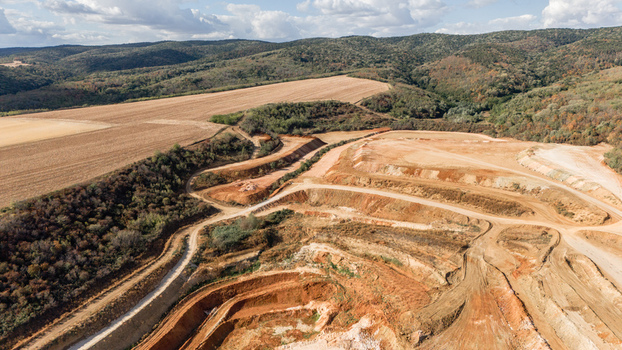 Aerial view of the open pit mine featuring terraced excavation dirt access roads and surrounding rural hills and agricultural fields in Besenovo Vojvodina Serbia. Aerial view of the open pit mine featuring terraced excavation dirt access roads and surrounding rural hills and agricultural fields in Besenovo Vojvodina Serbia.