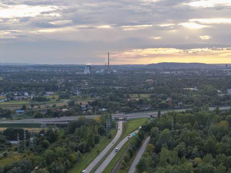 Aerial view of a highway stretching through lush greenery towards an industrial plant with cooling towers under a sunset sky in Krakow Lesser Poland Voivode Poland.