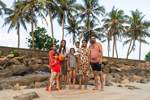 Sri Lanka 15 January 2026 View of a local family posing together on a sandy beach with large rocks and tall palm trees under a clear sky.