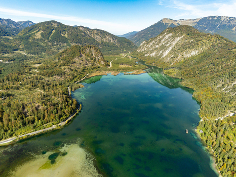 Aerial view of the Attensee lake surrounded by dense forests and rugged mountains under a clear blue sky in Rottenbach Bayern Germany. Aerial view of the Attensee lake surrounded by dense forests and rugged mountains under a clear blue sky in Rottenbach Bayern Germany.