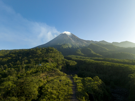 Aerial view of Bunker Kaliadem Merapi with lush green forests and a smoking volcanic peak under a clear blue sky in Kecamatan Pakem Daerah Istimewa Yogya Indonesia. Aerial view of Bunker Kaliadem Merapi with lush green forests and a smoking volcanic peak under a clear blue sky in Kecamatan Pakem Daerah Istimewa Yogya Indonesia.