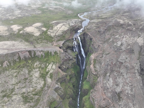 Aerial view of Glymur Waterfall cascading through a deep canyon with rugged cliffs mossy green terrain and a winding river in Bifrost Borgarbyggd Iceland.