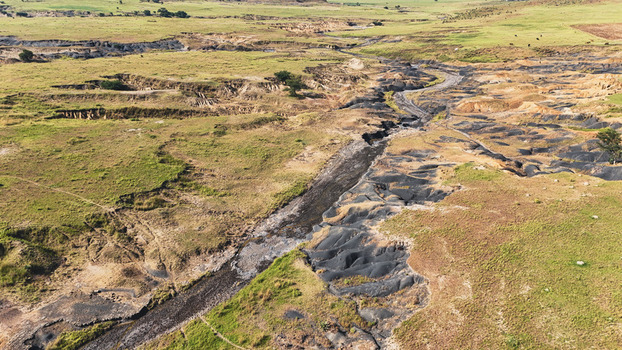 Aerial view of soil erosion and a deep donga cutting through the grassy landscape under bright sunlight Pietermaritzburg KwaZulu Natal South Africa.