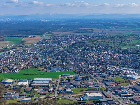 Aerial view of the sprawling cityscape nestled amidst verdant fields and distant hazy mountains a blend of urban and rural textures Sausheim Grand Est France.