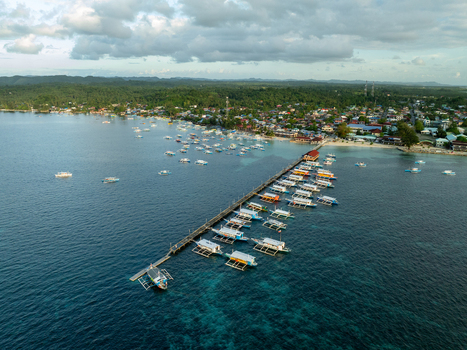 Aerial view of a long pier with numerous outrigger boats docked in clear turquoise water near a coastal town in Siargao Philippines. Aerial view of a long pier with numerous outrigger boats docked in clear turquoise water near a coastal town in Siargao Philippines.