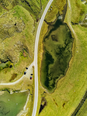 Aerial view of Silvretta Hochalpenstrasse winding through the lush green alpine landscape with a small lake and parked cars in Partenen Vorarlberg Austria. Aerial view of Silvretta Hochalpenstrasse winding through the lush green alpine landscape with a small lake and parked cars in Partenen Vorarlberg Austria.