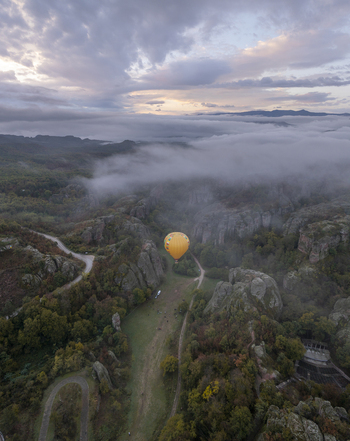 Aerial view of a yellow hot air balloon floating over the unique rock formations of Belogradchik surrounded by forests and low hanging clouds in Belogradchik Vidin Bulgaria.