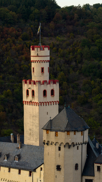Aerial view of the historic Marksburg castle tower with its distinctive red trimmed stone walls and flag set against a backdrop of dense forest in Braubach Rhineland Palatinate Germany. Aerial view of the historic Marksburg castle tower with its distinctive red trimmed stone walls and flag set against a backdrop of dense forest in Braubach Rhineland Palatinate Germany.