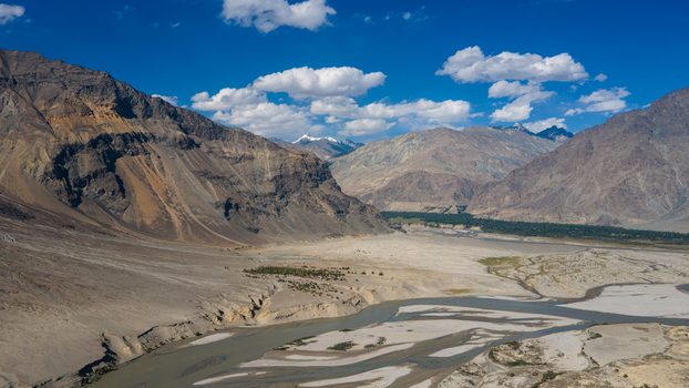 Aerial view of Shigar River flowing through the rugged mountain landscape with sandy riverbanks and rocky slopes under a bright blue sky in Skardu Gilgit Pakistan.