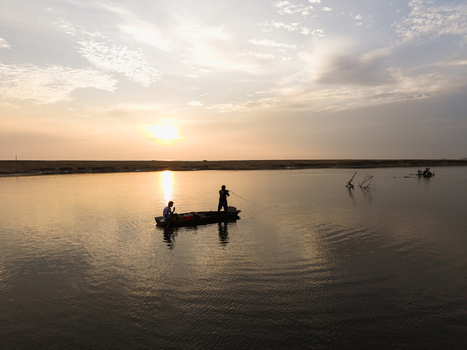 Aerial view of fishermen in a small wooden boat on calm water during a golden sunset with soft clouds Galle Southern Province Sri Lanka. Aerial view of fishermen in a small wooden boat on calm water during a golden sunset with soft clouds Galle Southern Province Sri Lanka.
