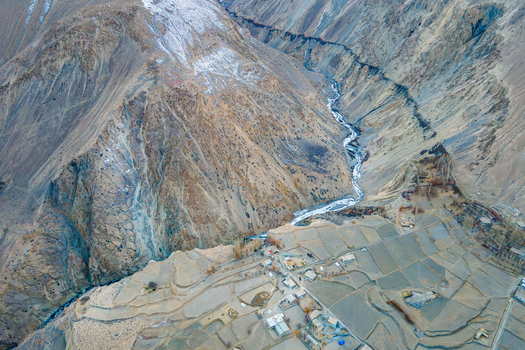 Aerial view of a river winding through rugged mountainous terrain meeting cultivated fields a stark contrast in textures and colors Hunza Nagar Gilgit Pakistan. Aerial view of a river winding through rugged mountainous terrain meeting cultivated fields a stark contrast in textures and colors Hunza Nagar Gilgit Pakistan.
