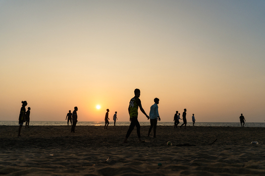 View of silhouettes of people walking and playing on a sandy beach during a vibrant sunset over the ocean in Galle Southern Province Sri Lanka.