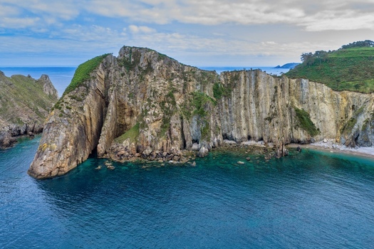 Aerial view of the dramatic vertical cliffs and turquoise waters at the Silence Beach Viewpoint with lush green vegetation in Cudillero Asturias Spain.