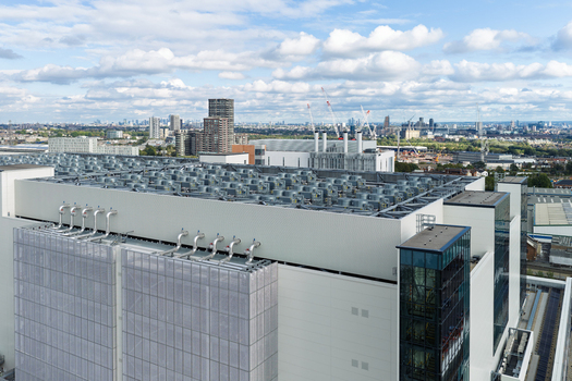 Aerial view of a large data center with numerous cooling units on the roof set against an urban skyline under a blue sky in the United Kingdom. Aerial view of a large data center with numerous cooling units on the roof set against an urban skyline under a blue sky in the United Kingdom.