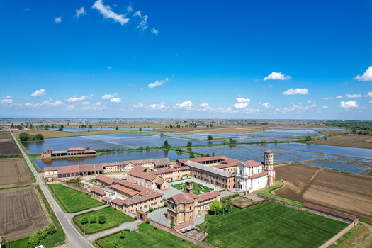Aerial view of the historic Abbazia di Lucedio complex surrounded by flooded rice fields and rural landscape under a blue sky in Trino Piemonte Italy.