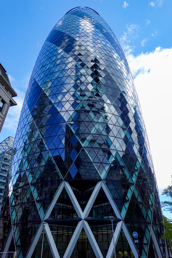 View of 30 St Mary Axe also known as The Gherkin featuring its iconic curved glass facade reflecting the blue sky in London England United Kingdom.