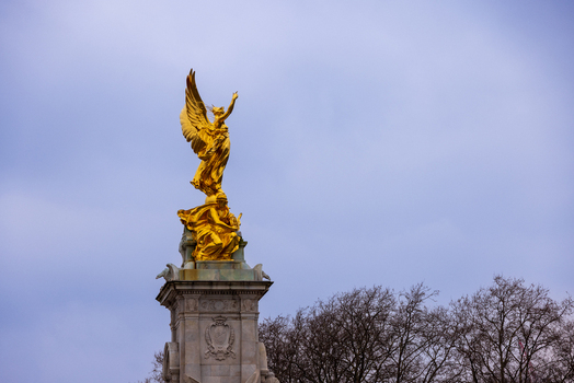 London United Kingdom 12 May 2025 View of the golden Victoria Memorial statue standing atop its stone pedestal against an overcast sky and bare trees.