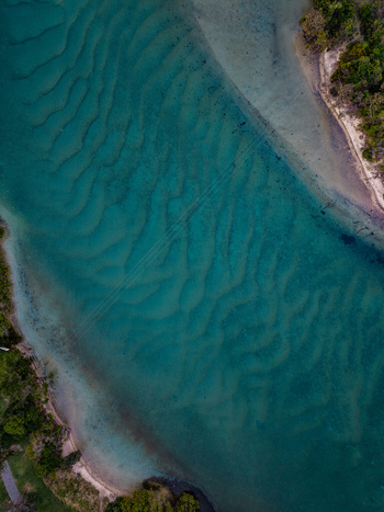 Aerial view of Cudgen Creek featuring clear turquoise water with visible sand ripples on the bed and lush vegetation along the banks in Tweed Shire Council New South Wales Australia.