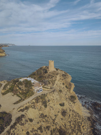 Aerial view of Torre del Xarco on a rocky cliff overlooking the Mediterranean Sea with a small building and a white van nearby La Vila Joiosa Comunidad Valenciana Spain.