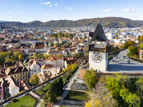 Aerial view of the iconic clock tower Grazer Uhrturm standing tall amidst the vibrant cityscape with its red rooftops Graz Styria Austria.