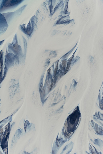 Aerial view of intricate braided river channels with glacial sediment flowing through dark volcanic terrain in Selfoss Sveitarfelagid Arborg Iceland. Aerial view of intricate braided river channels with glacial sediment flowing through dark volcanic terrain in Selfoss Sveitarfelagid Arborg Iceland.