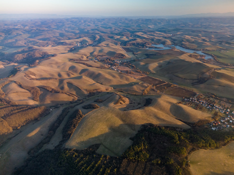 Aerial view of rolling hills bathed in the warm glow of the setting sun revealing a textured landscape of browns and greens Cerova vrchovina Slovakia.