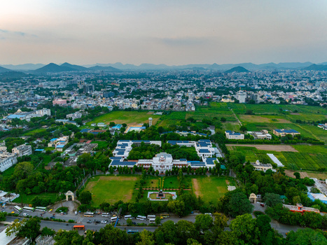 Aerial view of a large institutional building complex surrounded by lush green lawns trees and agricultural fields with the cityscape of Udaipur Rajasthan India. Aerial view of a large institutional building complex surrounded by lush green lawns trees and agricultural fields with the cityscape of Udaipur Rajasthan India.