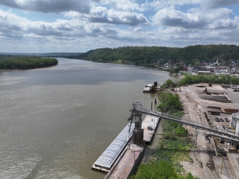 Aerial view of an industrial barge loading facility on the banks of the Ohio River with forested hills and the town skyline under a cloudy sky Aurora Indiana United States. Aerial view of an industrial barge loading facility on the banks of the Ohio River with forested hills and the town skyline under a cloudy sky Aurora Indiana United States.