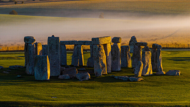 Aerial view of the prehistoric monument Stonehenge featuring ancient standing stones illuminated by golden hour light amidst a misty landscape in Salisbury England United Kingdom. Aerial view of the prehistoric monument Stonehenge featuring ancient standing stones illuminated by golden hour light amidst a misty landscape in Salisbury England United Kingdom.