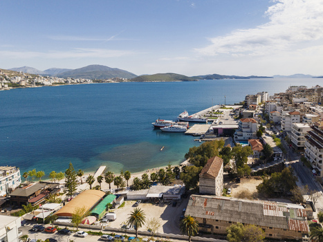 Aerial view of the coastal city of Saranda with its harbor ferries urban buildings palm trees and mountains in the background Saranda Vlore County Albania. Aerial view of the coastal city of Saranda with its harbor ferries urban buildings palm trees and mountains in the background Saranda Vlore County Albania.