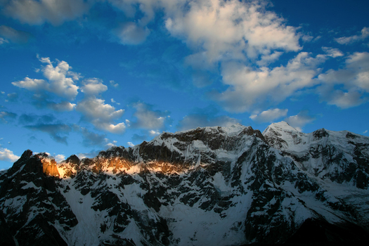 View of the snow capped peaks of the Goro II campsite illuminated by golden sunlight under a blue sky in Gilgit Pakistan. View of the snow capped peaks of the Goro II campsite illuminated by golden sunlight under a blue sky in Gilgit Pakistan.
