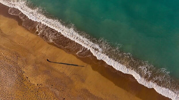 Aerial view of Manavgat Mendirek beach with turquoise sea waves washing onto the golden sand and a person walking casting a long shadow in Manavgat Antalya Turkiye.