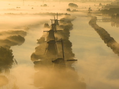 Aerial view of the historic windmills of Unesco World Heritage Kinderdijk shrouded in thick morning mist along a canal during golden hour Kinderdijk Zuid Holland Netherlands.