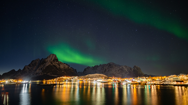 Nordland Norway 21 September 2026 Aerial view of Lofoten at night with the green Aurora Borealis over snow capped mountains and a glowing coastal village reflected in the water. Nordland Norway 21 September 2026 Aerial view of Lofoten at night with the green Aurora Borealis over snow capped mountains and a glowing coastal village reflected in the water.