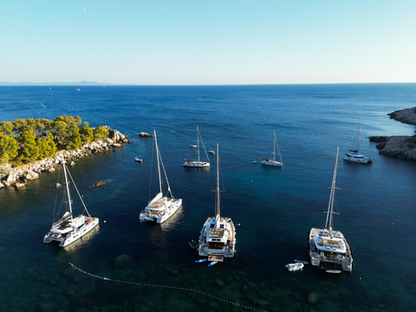 Aerial view of catamarans and sailboats anchored in the clear blue waters of a bay near Hvar surrounded by pine covered rocky coastlines in Split Dalmatia County Croatia.