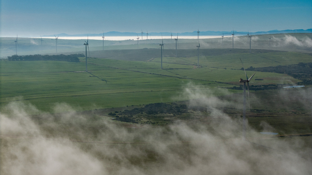 Aerial view of wind turbines standing in a rolling green landscape partially covered by morning mist in Vredenburg Western Cape South Africa. Aerial view of wind turbines standing in a rolling green landscape partially covered by morning mist in Vredenburg Western Cape South Africa.