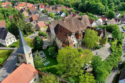 Aerial view of Schloss Wiesenthau with its historic towers and red tiled roofs surrounded by lush green trees and village houses Wiesenthau Bayern Germany. Aerial view of Schloss Wiesenthau with its historic towers and red tiled roofs surrounded by lush green trees and village houses Wiesenthau Bayern Germany.