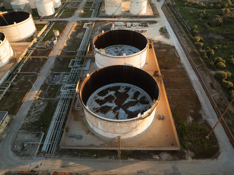 Aerial view of large industrial storage tanks and complex piping systems at a refinery facility under warm sunlight in Augusta Sicily Italy. Aerial view of large industrial storage tanks and complex piping systems at a refinery facility under warm sunlight in Augusta Sicily Italy.