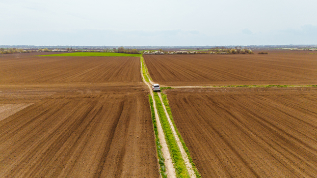 Aerial view of a lone vehicle driving along a dirt road bisecting vast ploughed fields with contrasting soil tones Sremska Mitrovica Vojvodina Serbia. Aerial view of a lone vehicle driving along a dirt road bisecting vast ploughed fields with contrasting soil tones Sremska Mitrovica Vojvodina Serbia.