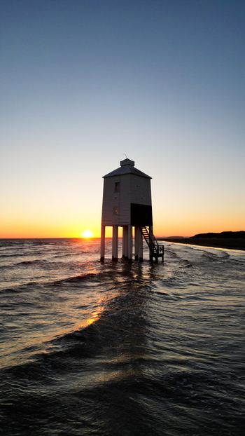 Aerial view of the Burnham on Sea Low Lighthouse on wooden stilts in the sea during a golden sunset with waves reflecting the light. Burnham on Sea England United Kingdom. Aerial view of the Burnham on Sea Low Lighthouse on wooden stilts in the sea during a golden sunset with waves reflecting the light. Burnham on Sea England United Kingdom.