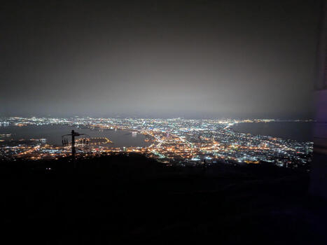 View of the illuminated cityscape of Hakodate at night seen from Mount Hakodate with glowing street lights and coastal harbor lights reflecting in the water Hakodate Hokkaido Japan.