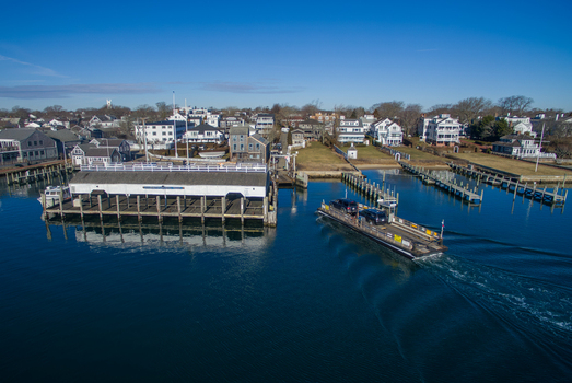 View of the Chappy Ferry carrying vehicles across the water towards the historic waterfront houses and docks of Martha s Vineyard Edgartown Massachusetts United States.