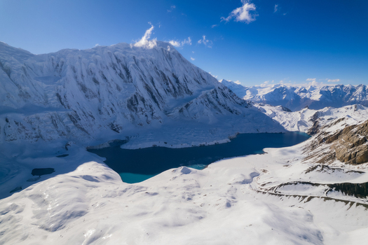 Aerial view of a snow covered mountain peak towering over a deep blue glacial lake in the Himalayas Nepal.