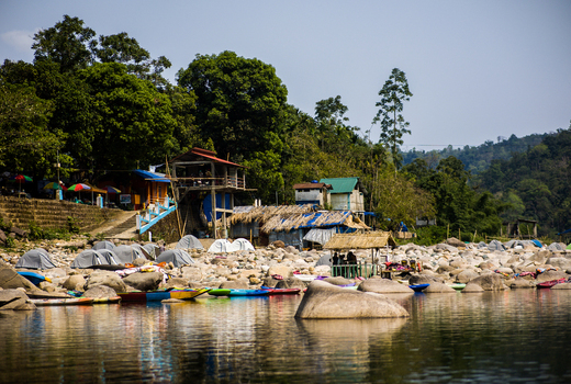 Meghalaya India 31 March 2023 View of a riverbank with colorful kayaks camping tents and small wooden structures nestled among lush green trees and large river rocks. Meghalaya India 31 March 2023 View of a riverbank with colorful kayaks camping tents and small wooden structures nestled among lush green trees and large river rocks.