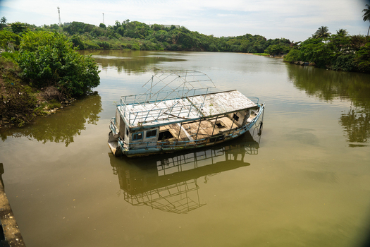 View of a dilapidated wooden boat floating in a calm lagoon surrounded by lush tropical vegetation and green hills Mirissa Southern Province Sri Lanka. View of a dilapidated wooden boat floating in a calm lagoon surrounded by lush tropical vegetation and green hills Mirissa Southern Province Sri Lanka.
